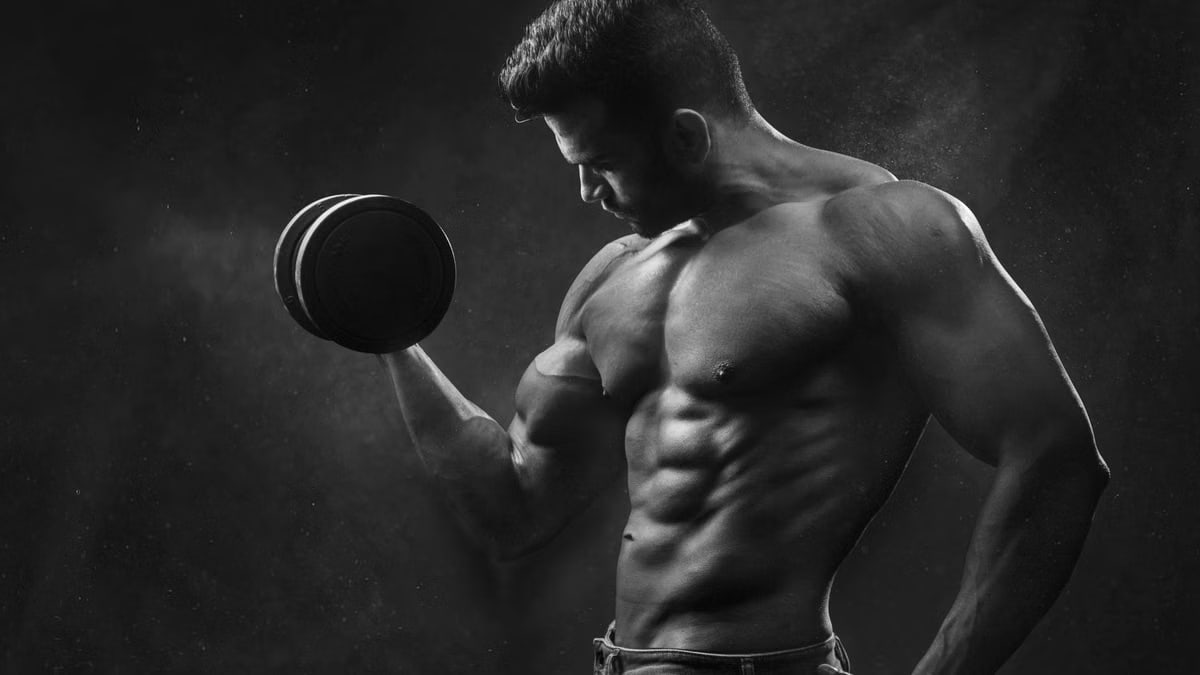 Powerful black and white portrait of a shirtless bodybuilder lifting dumbbells in the gym.